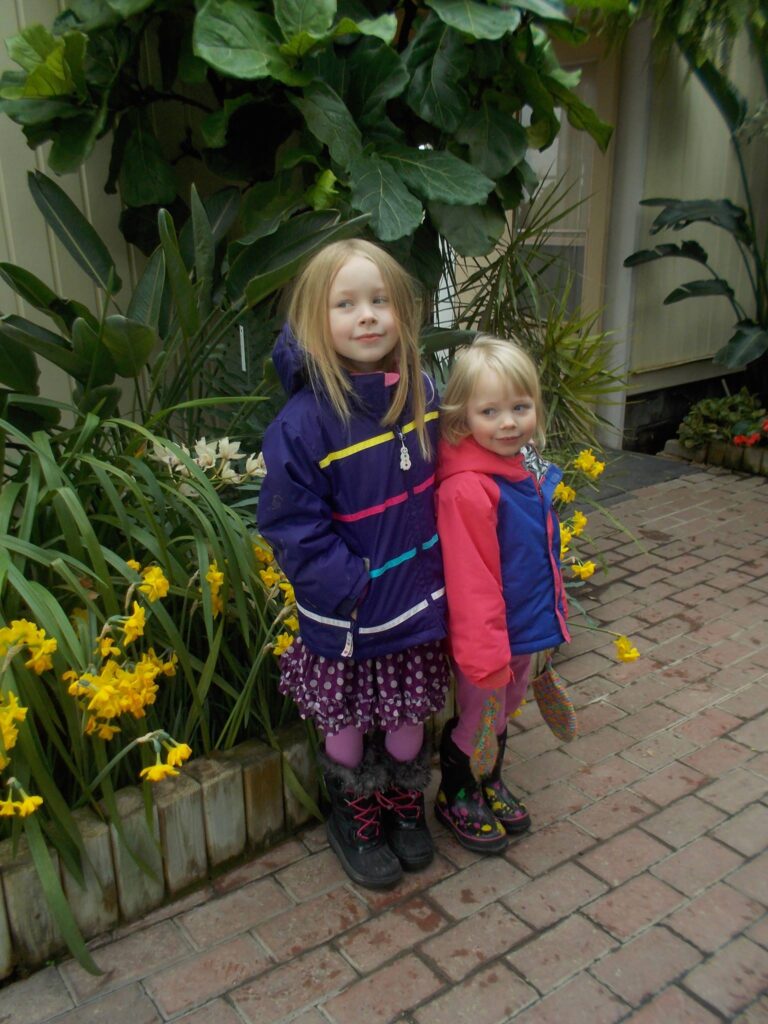 Two female children stand in front of blooming flowers and greenery at the City of Kingston greenhouse.